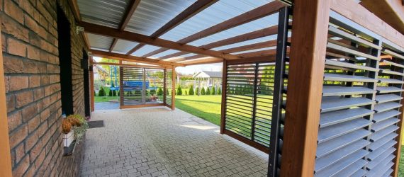 Zadaszenie tarasu z drewnianą konstrukcją i ruchomymi żaluzjami shutters zapewniającymi regulację światła, poliwęglanowe pokrycie dachu Fastlock.