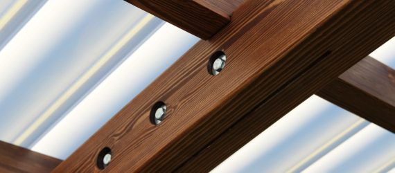 Detal konstrukcyjny brązowych drewnianych belek z wkrętami jako część zadaszenia tarasu